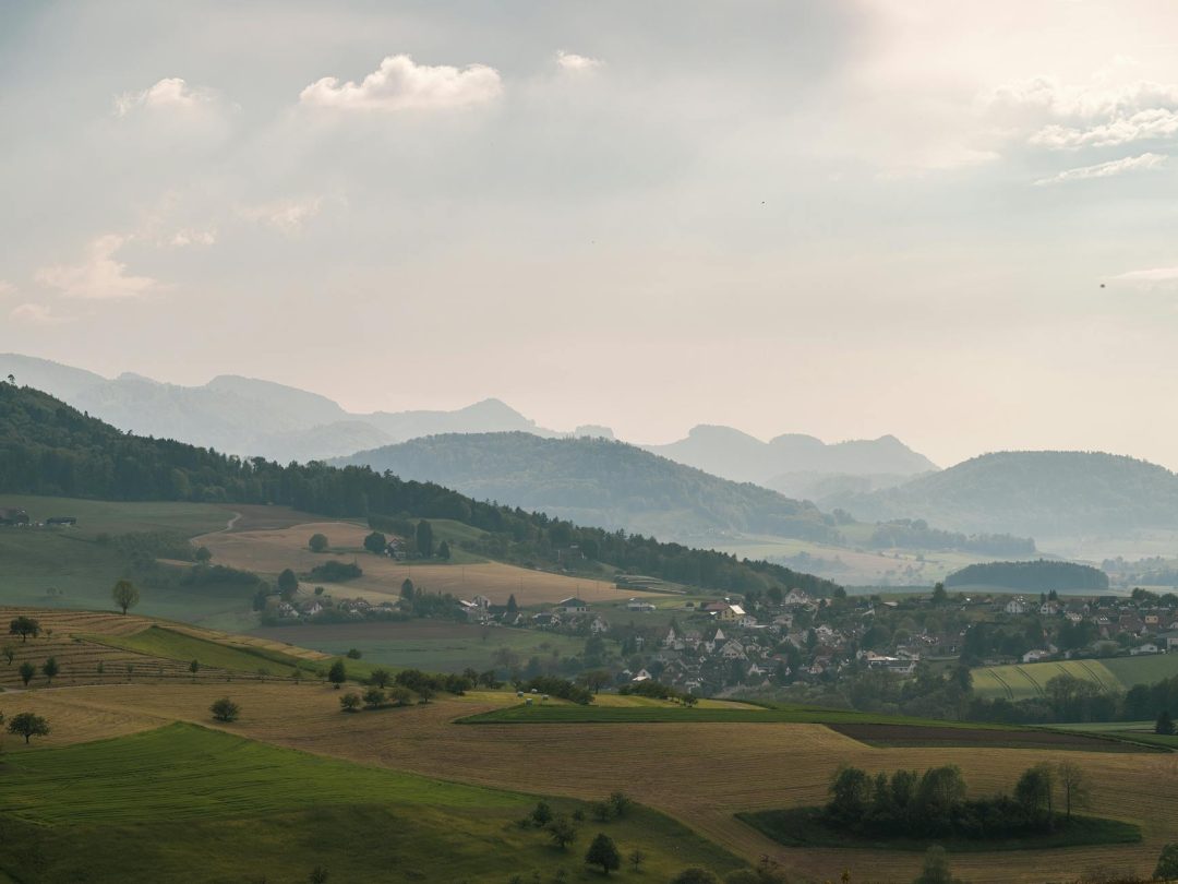 Aerial view of a peaceful countryside with rolling hills and fog in the distance, perfect for a tranquil escape.