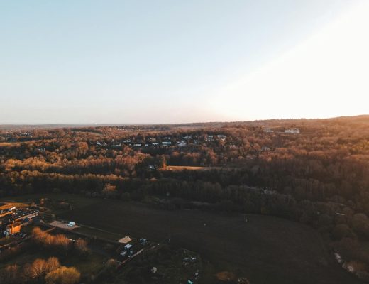A scenic aerial shot over the English countryside at sunset showcasing houses and a vast forest.