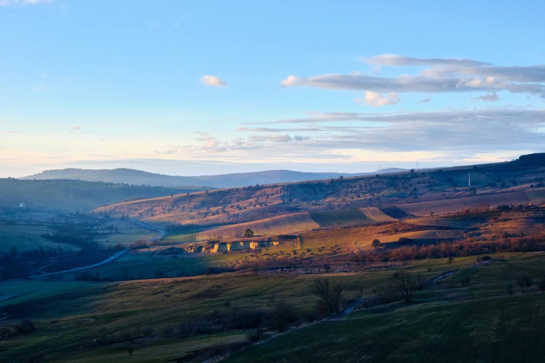 Beautiful landscape of rolling hills with soft sunset lighting and scattered clouds.