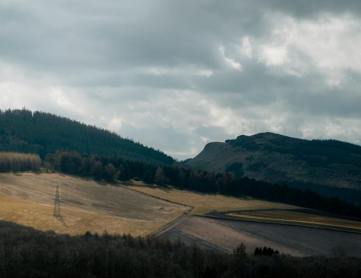 A tranquil mountain landscape with fields and cloudy sky, creating a dramatic scene.