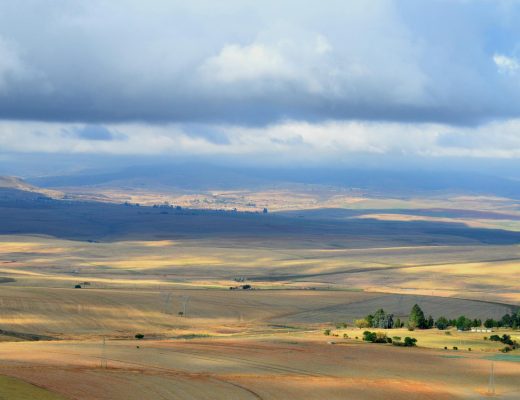 Vast South African landscape with fields under a cloudy sky, showcasing nature's beauty.