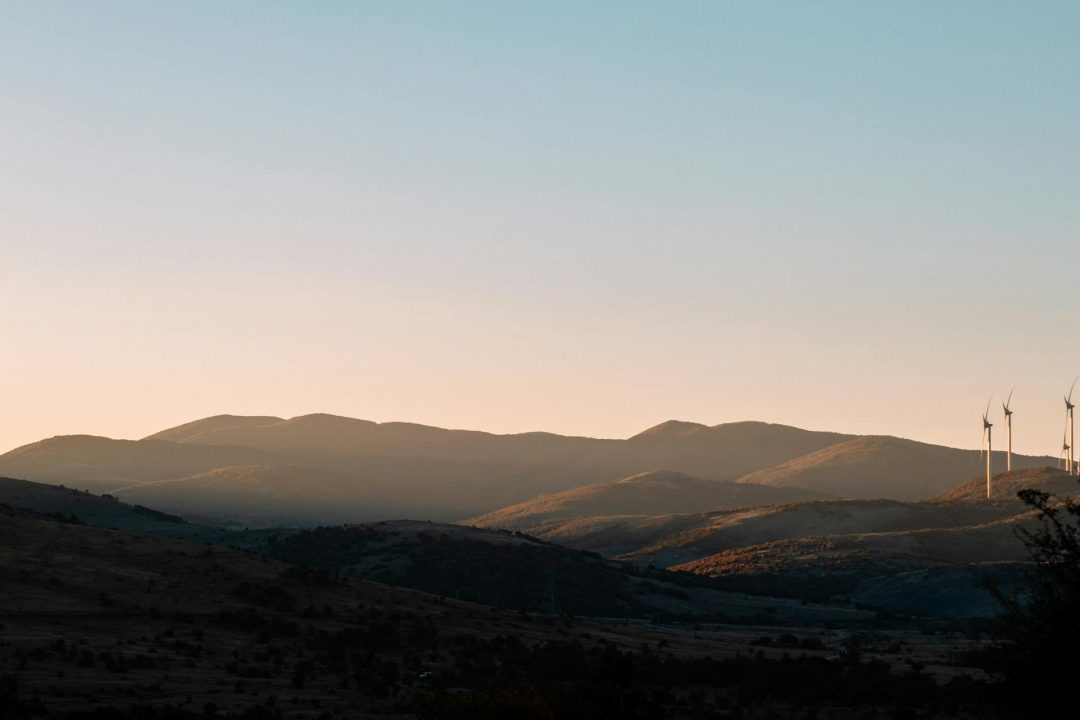 Beautiful landscape at sunset with wind turbines silhouetted against rolling hills, showcasing renewable energy in nature.