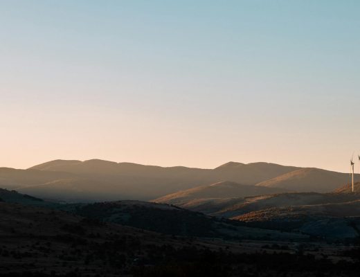Beautiful landscape at sunset with wind turbines silhouetted against rolling hills, showcasing renewable energy in nature.