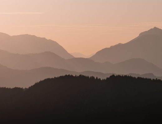 Tranquil mountain layers with pastel skies captured at sunrise, providing a serene background scene.