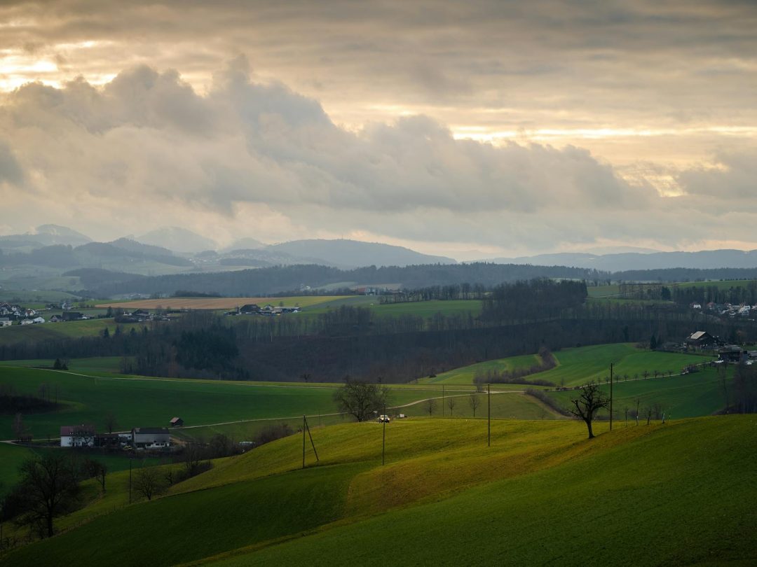 Breathtaking view of rolling hills and fields under a dramatic sunset sky.
