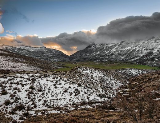 Breathtaking view of a snow-covered mountain valley with dramatic skies at sunset.
